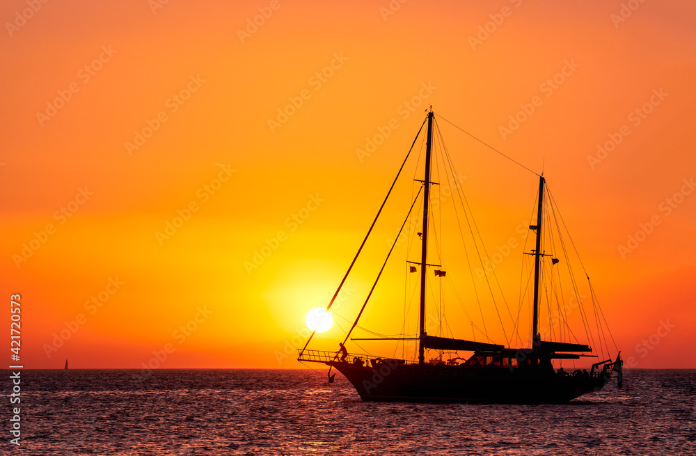 Silhouette of sailing boat with sails down against sun at sunset, sun glare on sea waters. Romantic seascape, sun touch headsail ropes.