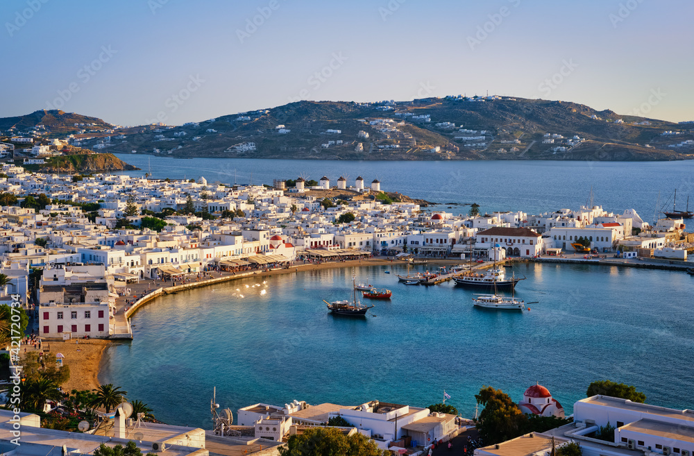 Beautiful sunset view over town of Mykonos, Greece and port. Golden hour, harbor, cruise ships, whitewashed houses. Vacations, Mediterranean lifestyle