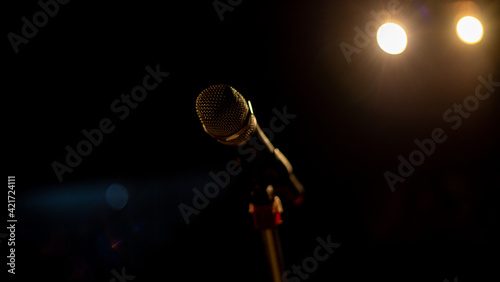 Side view of micrphone on stand sitting on empty stage with lights shinning in background