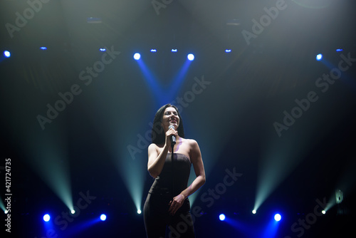 Singer perform on stage of nightclub in front of bright screen. Dark background, smoke, concert spotlights