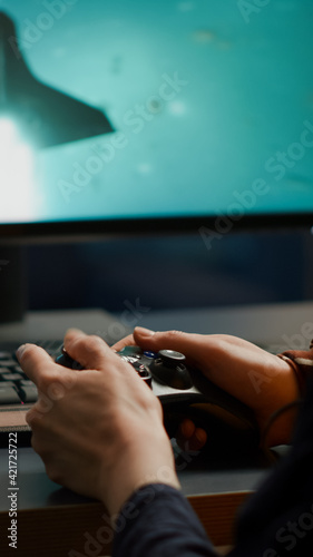 Closeup of competitive woman player holding joystick playing space shooter video games at powerful computer late night. Professional gamer using wireless controller for online gaming championship