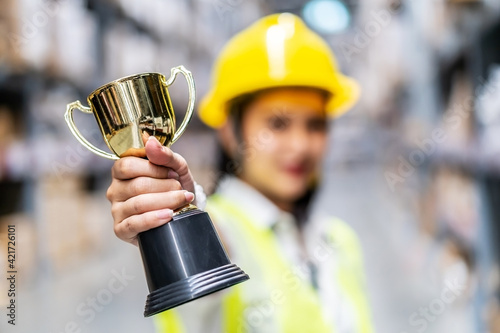 Fotografie Happy woman warehouse worker holding a trophy after being selected as an outstan