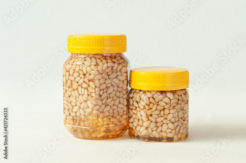 Pine nut with honey in a transparent jar with a yellow lid. A smaller jar with nuts and honey is next to it. Place for a label. Close-up. Light background.