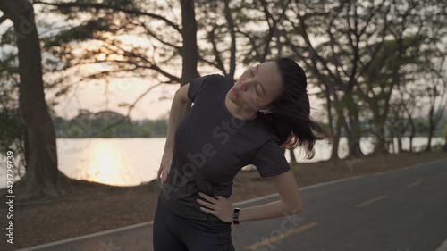 asian athlete woman in black sportswear stretching muscle warm up body for exercise and prevent injury at green lake park in sunset.