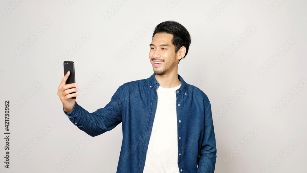 Video call conference, Happy asian man having a video chat on mobile phone while standing on grey background, Asia male talking video call on a smartphone, Social distancing Video call conference, Happy asian man having a video chat on mobile phone while standing on grey background, Asia male talking video call on a smartphone, Social distancing