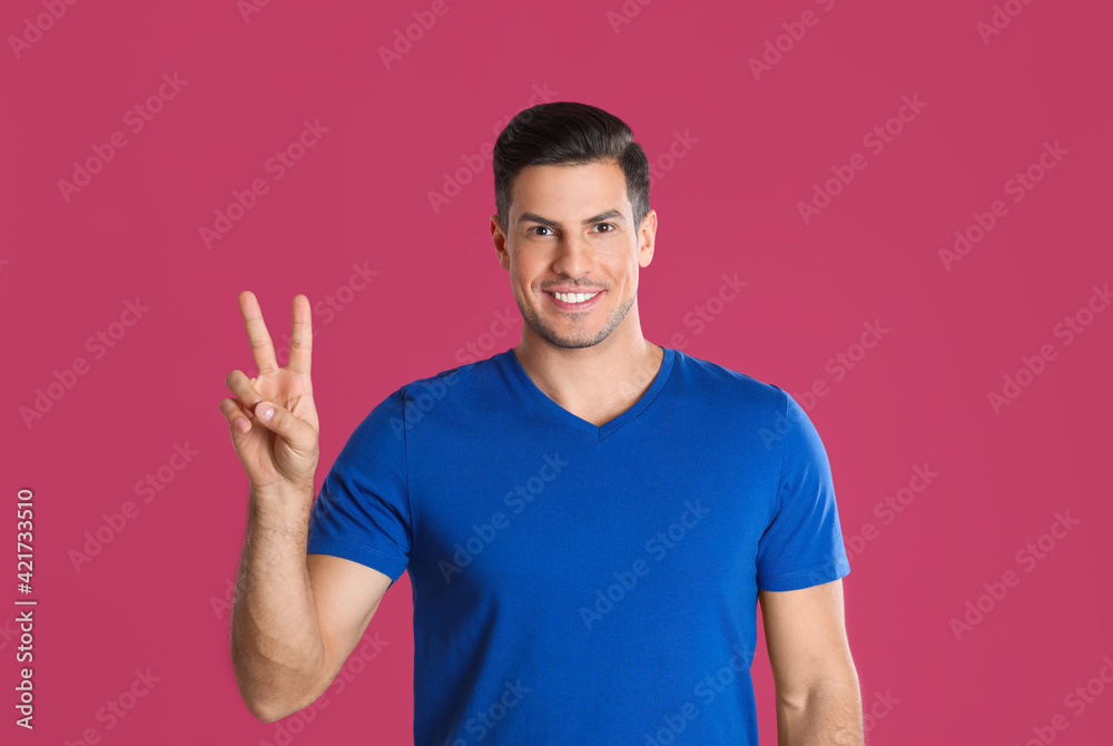 Man showing number two with his hand on pink background