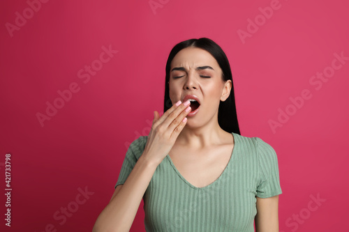 Young tired woman yawning on pink background