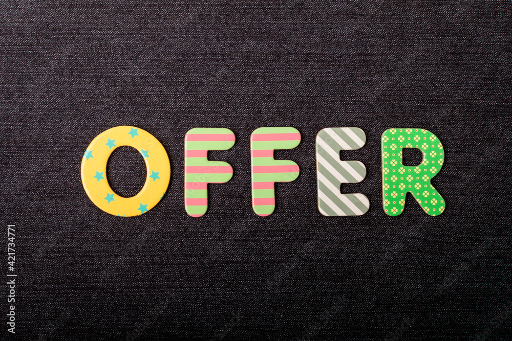 Card with Offer word made from mixed vivid colored wooden letters on a textured dark black textile material that can be used as a message. Card with Offer word made from mixed vivid colored wooden letters on a textured dark black textile material that can be used as a message.