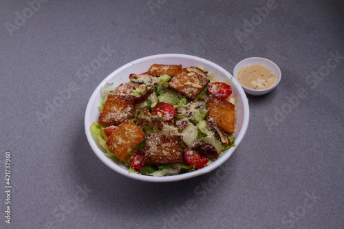 Bowl of traditional caesar salad with chicken and bacon isolated on gray background
