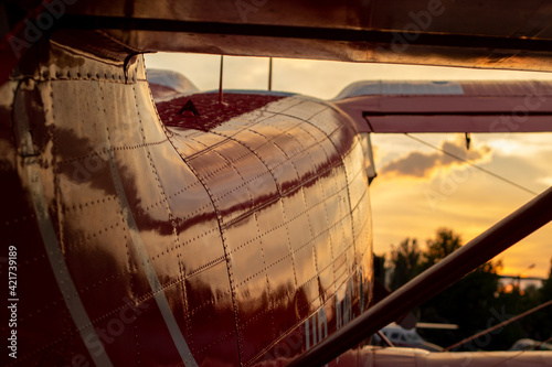 Part of the shiny hull of a red small-passenger plane in sunset light