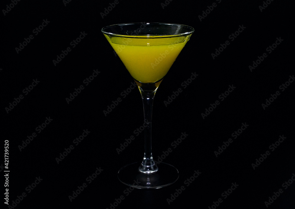 A tequila glass with a yellow cocktail on a black background.