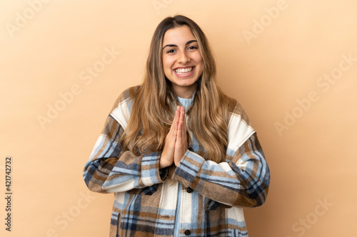 Young caucasian woman isolated on beige background keeps palm together. Person asks for something