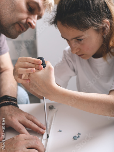 Cute caucasian girl and her beautiful father are assembling furniture with a screewdriver. Housework. Front view. Vertical shot. Close-up photo