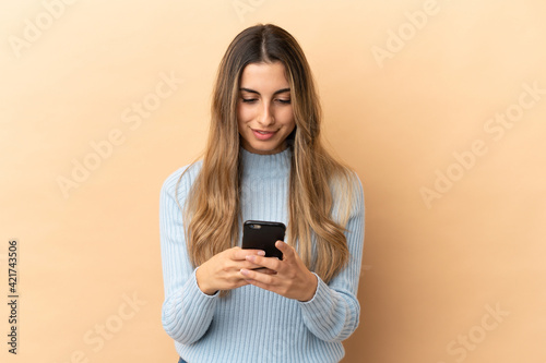 Young caucasian woman isolated on beige background sending a message with the mobile