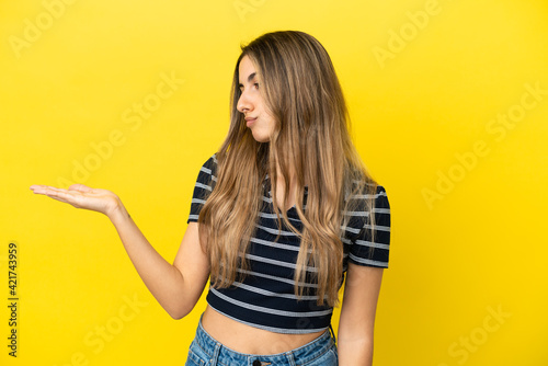 Young caucasian woman isolated on yellow background holding copyspace with doubts © luismolinero