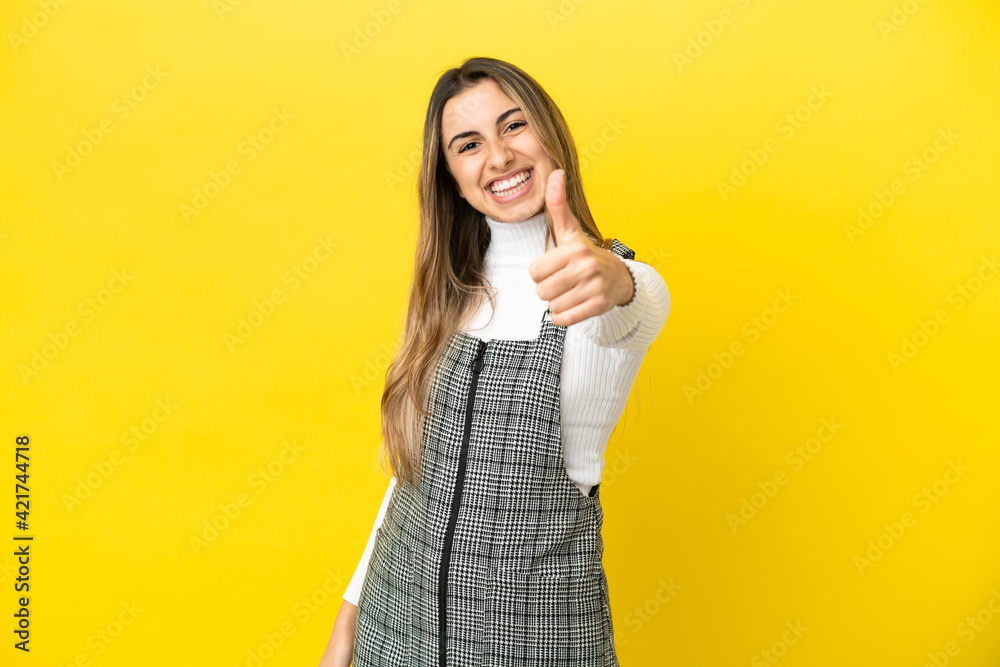 Young caucasian woman isolated on yellow background with thumbs up because something good has happened Young caucasian woman isolated on yellow background with thumbs up because something good has happened