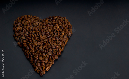 Roasted arabica coffee beans laid out in the shape of a heart, lie on a dark wooden background close up