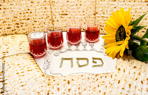 Pesah celebration concept - Jewish Passover holiday. Top view on traditional unleavened bread food - matzoh, glasses with red wine and sunflower. Letters, in translation mean as Jewish Passover photo