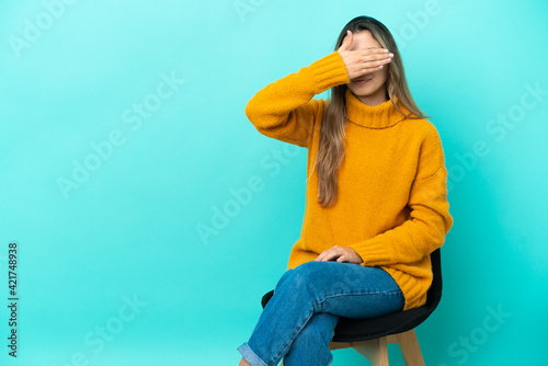 Young caucasian woman sitting on a chair isolated on blue background covering eyes by hands. Do not want to see something