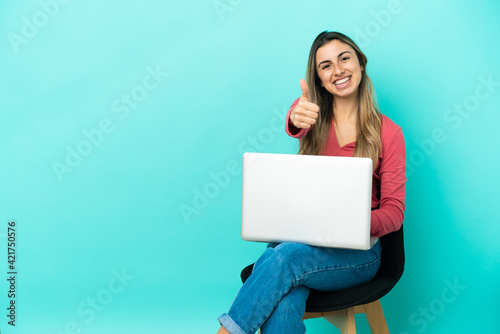 Young caucasian woman sitting on a chair with her pc isolated on blue background with thumbs up because something good has happened © luismolinero