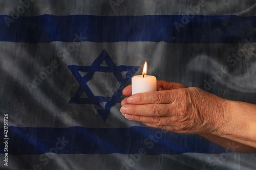 Hands hold a burning candle against the background of the flag of Israel. Day of Remembrance