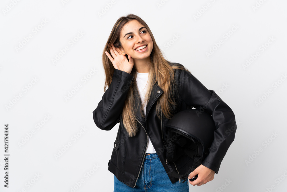Young Woman holding a motorcycle helmet over isolated white background listening something Young Woman holding a motorcycle helmet over isolated white background listening something