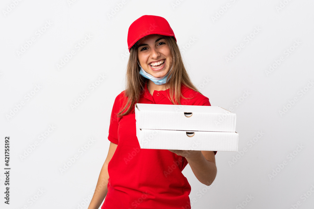 Pizza delivery woman holding a pizza and protecting from the coronavirus with a mask over isolated white wall with happy expression Pizza delivery woman holding a pizza and protecting from the coronavirus with a mask over isolated white wall with happy expression