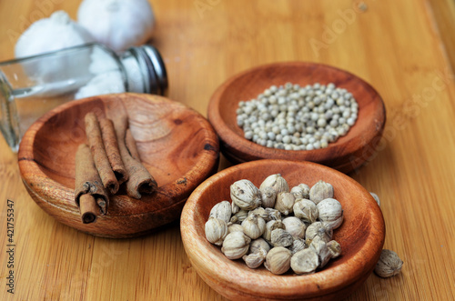 pepper, cardamom, and cinnamon in a wooden bowl on a wooden tray plus garlic and salt. close up with selective focus
