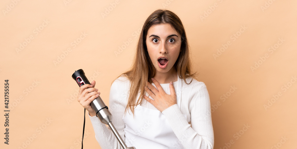 Woman using hand blender over isolated background surprised and shocked while looking right Woman using hand blender over isolated background surprised and shocked while looking right