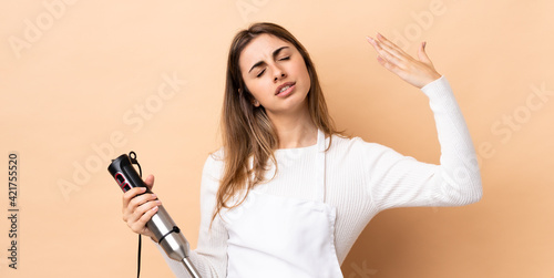 Woman using hand blender over isolated background with tired and sick expression