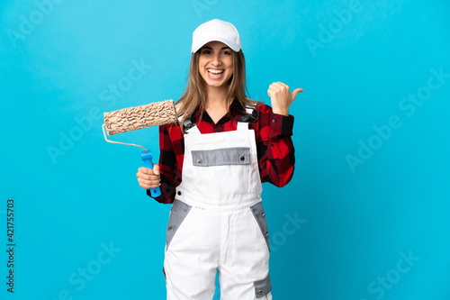 Painter woman over isolated blue background pointing to the side to present a product