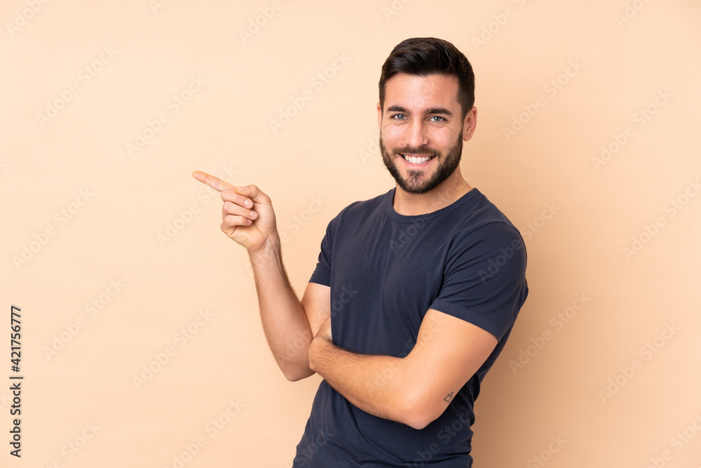 Caucasian handsome man isolated on beige background pointing finger to the side Caucasian handsome man isolated on beige background pointing finger to the side