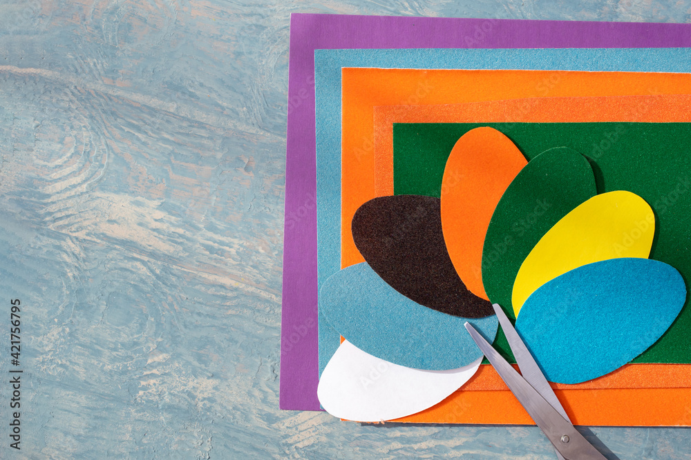Fototapeta premium Cut out colored Easter paper eggs, pattern and scissors on colorful paper on a blue wooden table, copy space