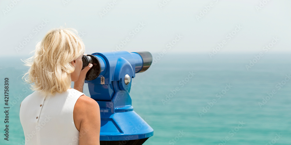 Adult woman looking through binocular viewer on the sea landscape, space for text. Europe destination.