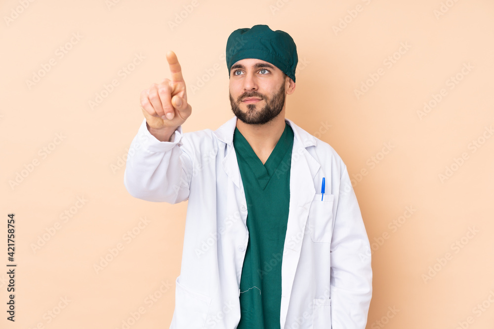 Surgeon man isolated on beige background touching on transparent screen Surgeon man isolated on beige background touching on transparent screen