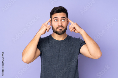 Caucasian handsome man having doubts and thinking over isolated purple background © luismolinero