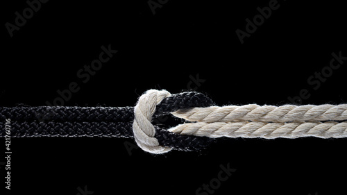 Black and white ropes are tied in a knot on a black background