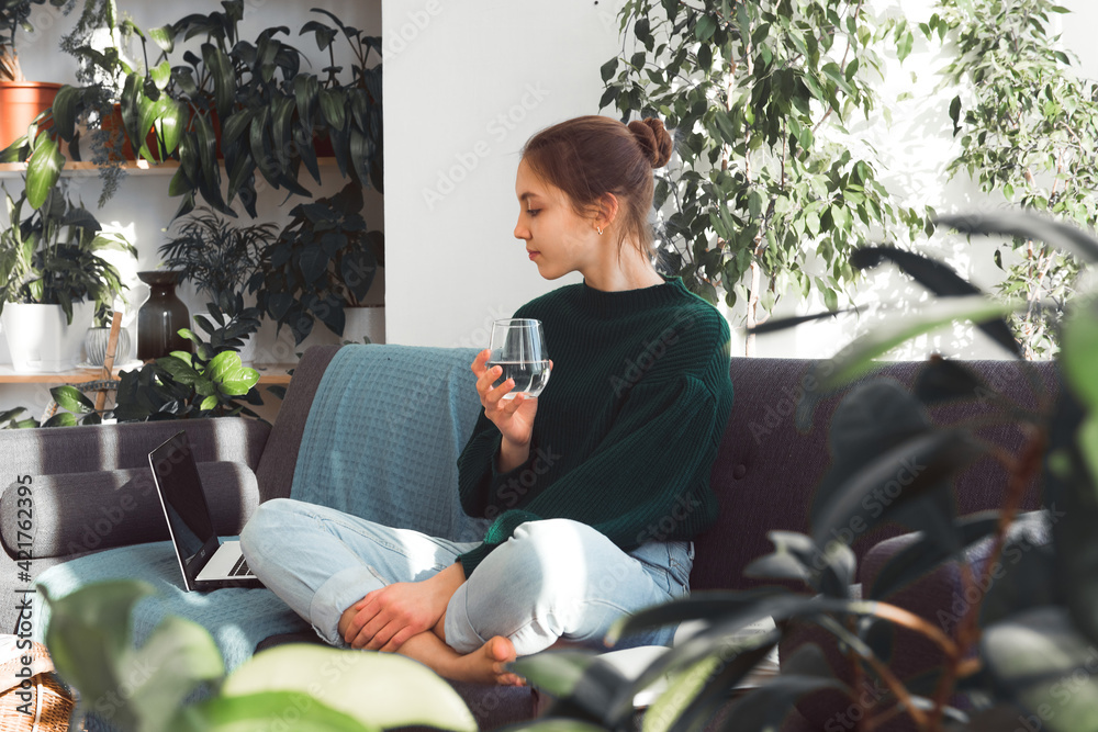 teen girl sit on sofa with laptop, drink water, homework or distance learning teen girl sit on sofa with laptop, drink water, homework or distance learning