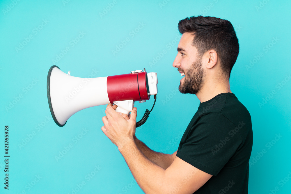 Caucasian handsome man isolated on blue background shouting through a megaphone Caucasian handsome man isolated on blue background shouting through a megaphone