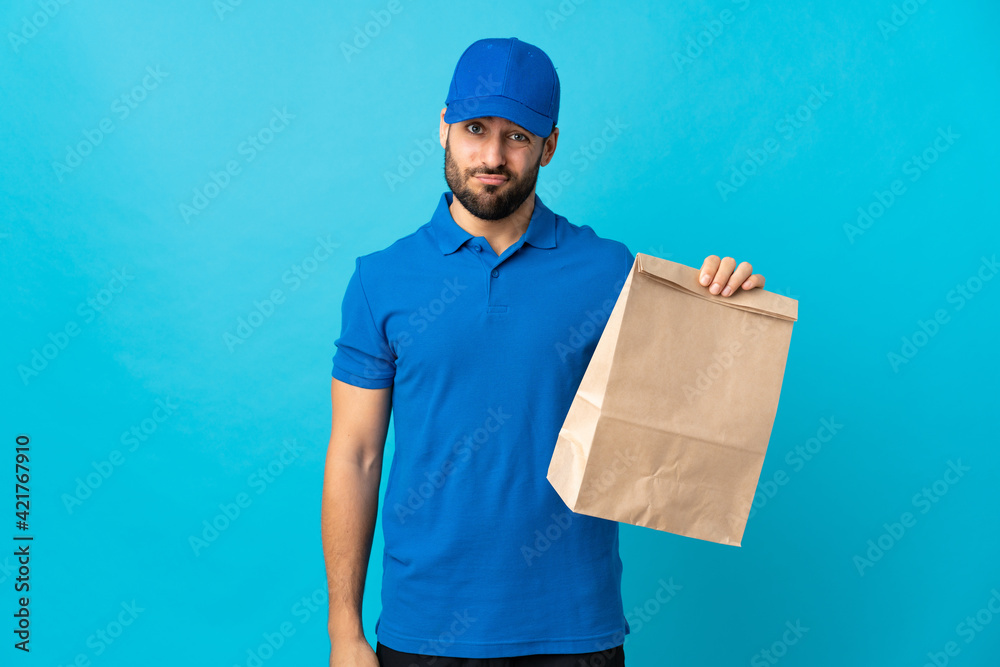 Delivery man with beard isolated on blue background with sad expression Delivery man with beard isolated on blue background with sad expression