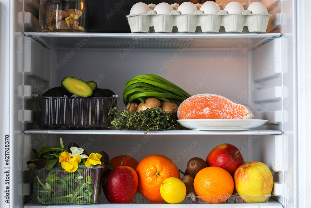 Open fridge with healthy food.Products on the shelves.Proper nutrition with red fish, avocado and fruits.Refrigerator with healthy products.Fruits, eggs, fish, avocado, mushrooms, herbs, kiwi, orange. Open fridge with healthy food.Products on the shelves.Proper nutrition with red fish, avocado and fruits.Refrigerator with healthy products.Fruits, eggs, fish, avocado, mushrooms, herbs, kiwi, orange.
