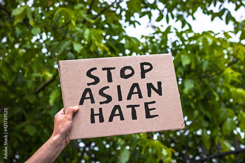 Hand holding cardboard banner with text STOP ASIAN HATE. Asian is not virus. Anti-racism protest. Stop hating or mistaking Asians for the cause of spreading of Covid-19. © hardvicore