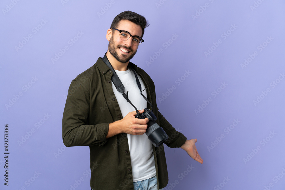 Obraz premium Photographer man over isolated purple background extending hands to the side for inviting to come