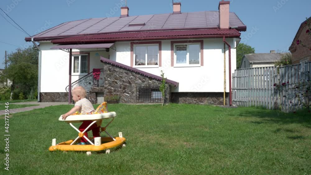 baby learns to walk on the background of the house,baby walks on the grass near his house in a walker baby learns to walk on the background of the house,baby walks on the grass near his house in a walker