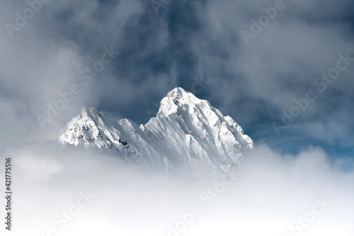 Obraz na płótnie Snowy snow-capped rock mountain peaks protrude from fog soup with a downward whi