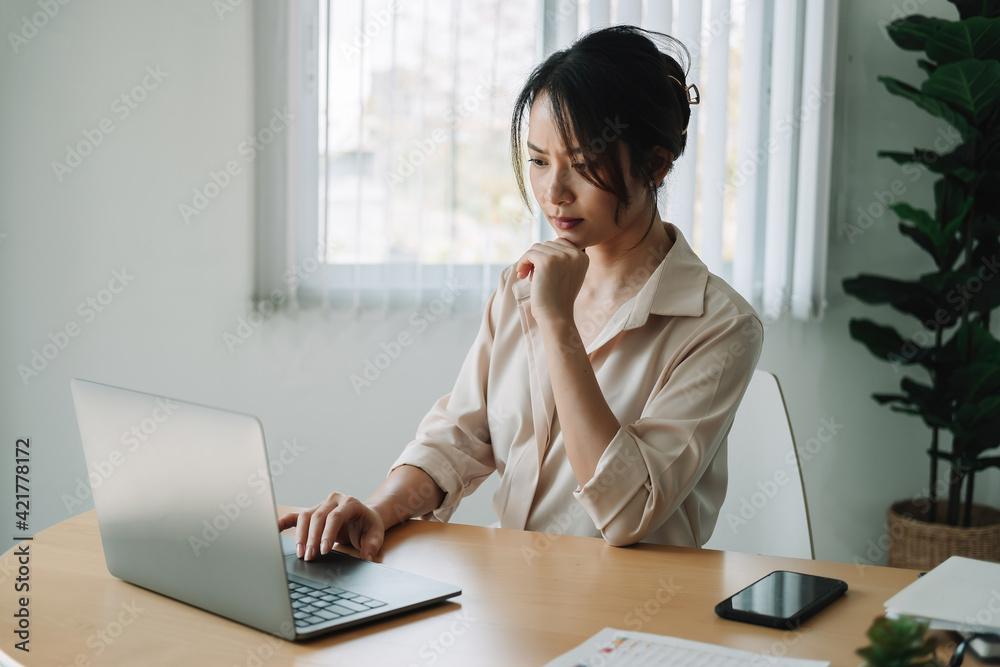 Young asian businesswoman thinking about something while sitting front open portable laptop computer reading email from client, long hours of work concept.
