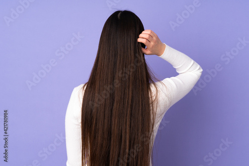 Young asian woman isolated on purple background in back position and thinking