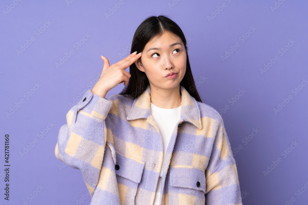 Young asian woman isolated on purple background with problems making suicide gesture