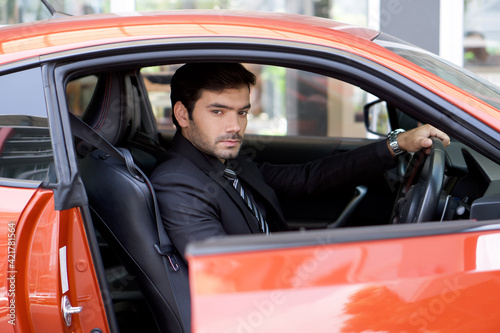 Young businessman in a black suit open sport car door while holding the wheel.