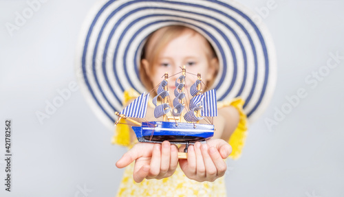 A girl in a wide-brimmed hat holds a toy boat in her hands.